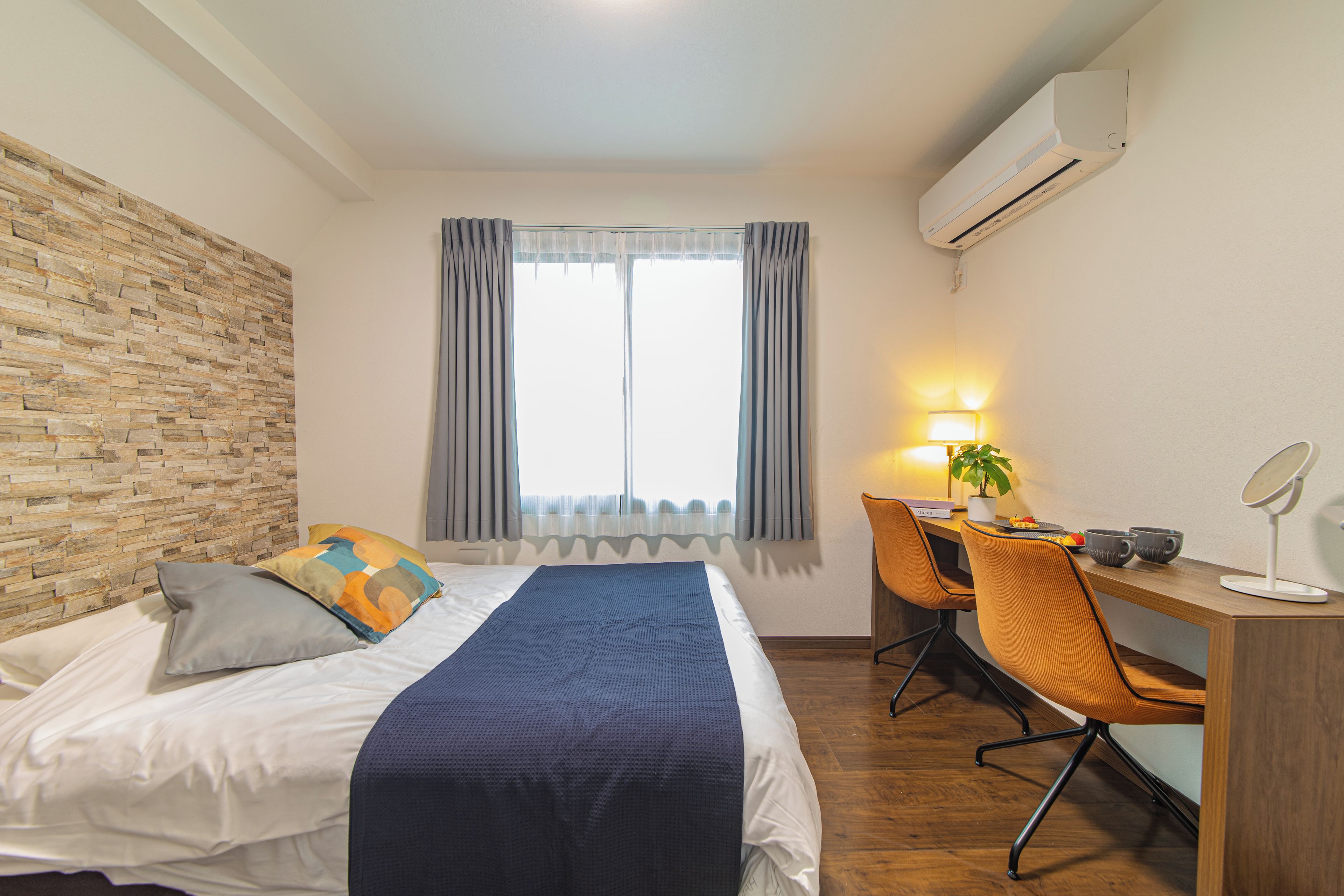 Een hotelkamer met een bed, een bureau, een stoel, een airconditioner en een raam met gordijnen.