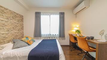 Een hotelkamer met een bed, een bureau, een stoel, een airconditioner en een raam met gordijnen.