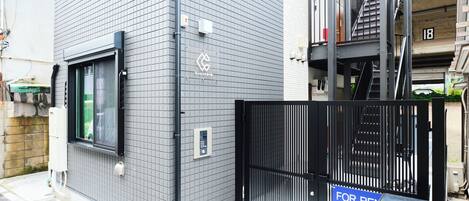 A modern building with a grey tiled facade, a black gate, and a 'For Rent' sign.