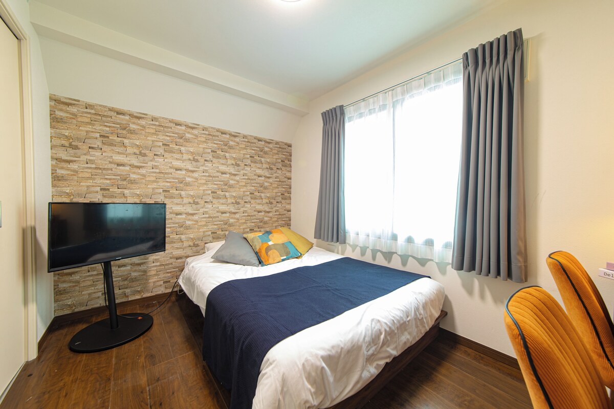 Ein Hotelzimmer mit Steinwand, einem Bett mit blauer Decke, einem Fernseher auf einem Schrank und einem Fenster mit Vorhängen.