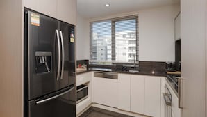 A compact kitchen with a black refrigerator, a dishwasher, and a window with blinds.