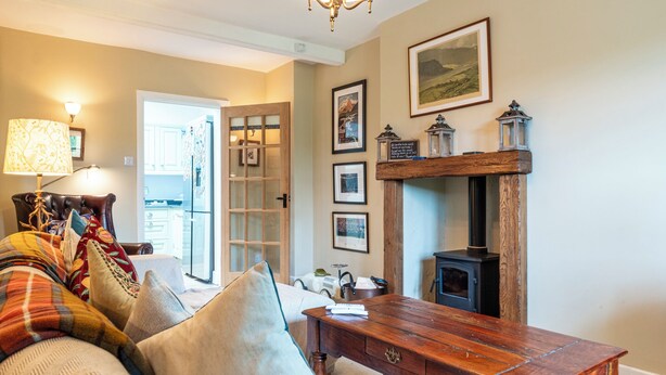 A cozy living room with a fireplace, a sofa with colorful cushions, a wooden coffee table, and a door leading to another room. - Beautiful 3BD Fam Retreat in Oxfordshire (Chipping Norton)