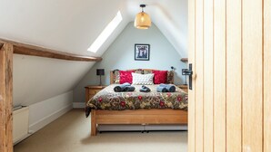 A bedroom with a sloped ceiling, a bed with a floral bedspread, red and white pillows, and a hanging light fixture. - Beautiful 3BD Fam Retreat in Oxfordshire (Chipping Norton)
