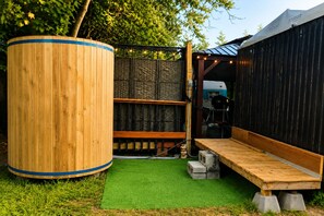 A wooden outdoor seating area with a green artificial turf, a large cylindrical object, and a black structure with a sloped roof.