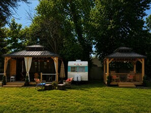 A covered outdoor seating area with chairs and tables, a covered porch, and a vintage camper parked in the background.