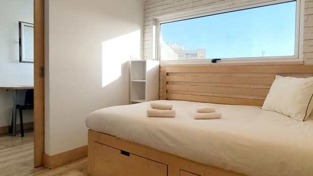 A bedroom with a wooden headboard, a large window, a desk, and a chair. - Cq15 Cozy Studio Next to HUC (Coimbra)