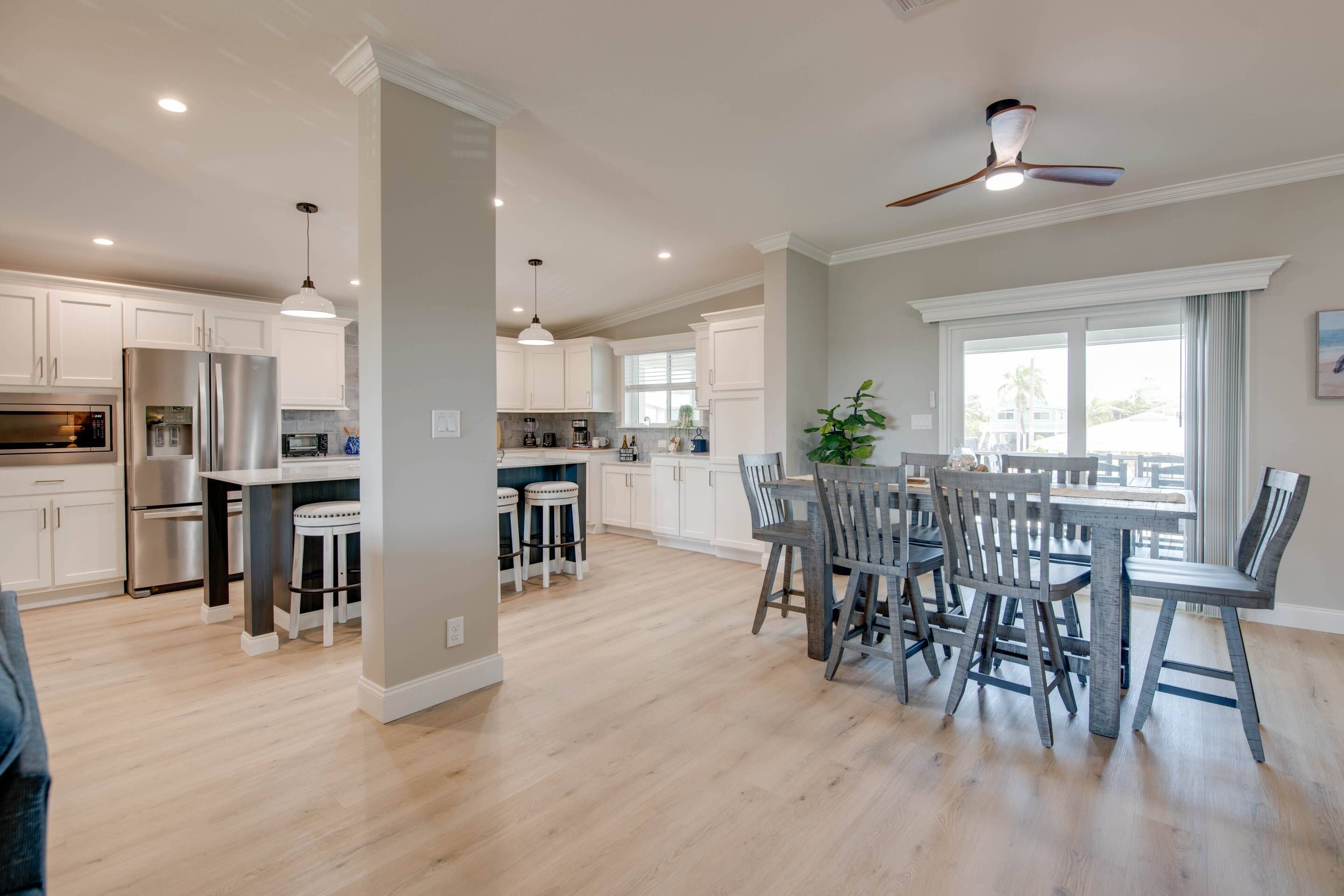 A spacious kitchen with white cabinets, a central island with stools, and a dining area with a table and chairs.