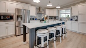 A modern kitchen with white cabinets, stainless steel appliances, and a central island with bar stools. - Big Pine Paradise: Beautiful Updated 4BR Canal Front Home, Pool, Dockage, Easy Gulf/Atlantic Access (Big Pine Key)