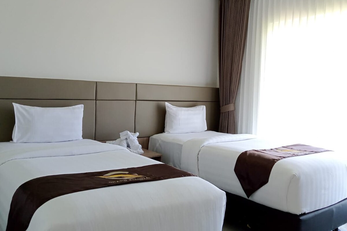 Ein Hotelzimmer mit zwei Betten, einem Kopfteil, einem Nachttisch, einem Telefon und einem Fenster mit Vorhängen.