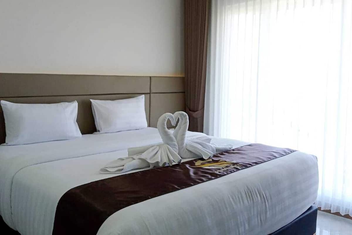 Ein Hotelzimmer mit einem ordentlich bezogenen Bett, einer Kopfteil und einem Fenster mit Vorhängen.