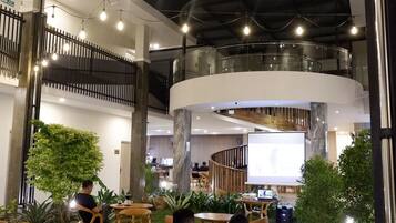 A modern indoor dining area with wooden tables and chairs, surrounded by greenery and a glass railing.