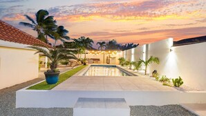 A modern outdoor pool area with a clear view of the sky, surrounded by palm trees and a well-maintained lawn.