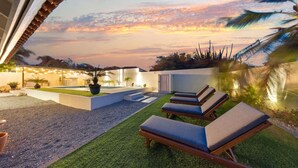 A rooftop terrace with lounge chairs, a small pool, and a view of the sunset.
