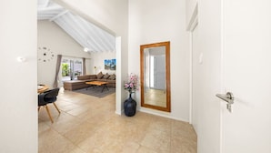 A spacious living area with a high ceiling, a dining table with chairs, a sofa, and a large mirror.