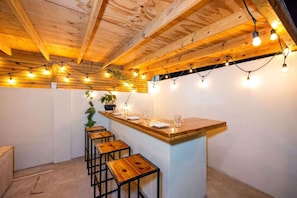 Un coin bar au style rustique, avec des tabourets en bois, un comptoir et des guirlandes lumineuses.