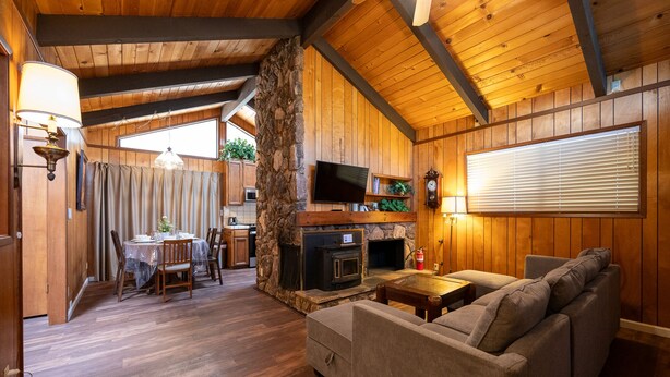 Ein gemütliches Blockhaus-Interieur mit Kamin aus Stein, Holzwänden, Essbereich und einer komfortablen Sitzecke.