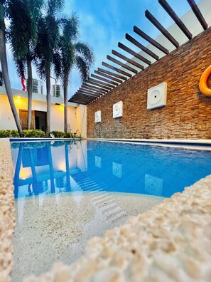 A swimming pool with a stone wall and wooden pergola. - Hubomoto People's Suite (Iloilo)