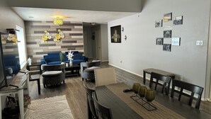 A modern living room with a blue sofa, grey armchairs, a wooden coffee table, and a dining area with a long table and benches. - Modern Cozy Retreat in Katy, TX (Katy)