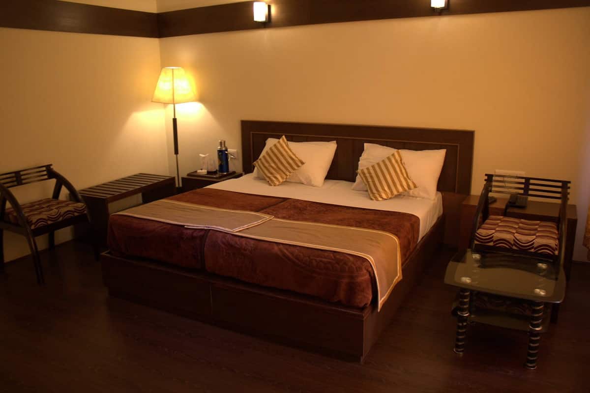 A hotel room with a large bed, two bedside tables, a lamp, and two chairs.