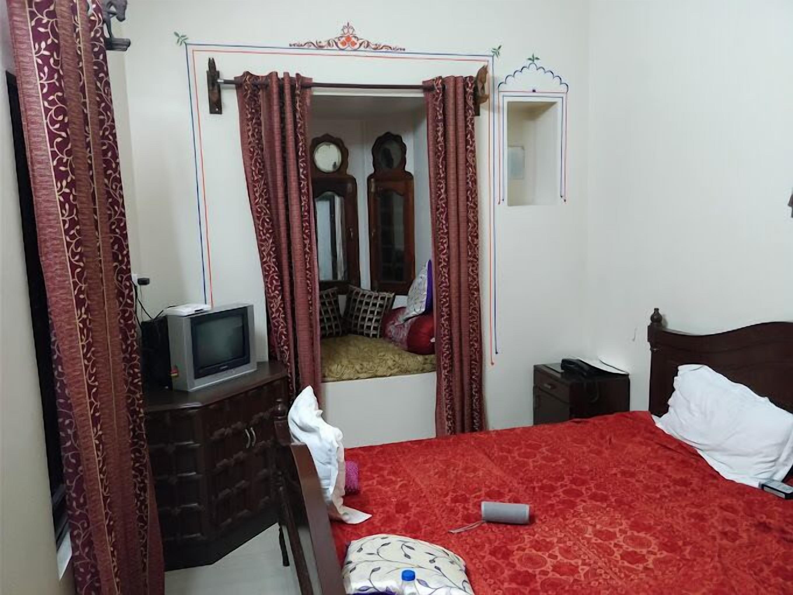 A bedroom with a bed, a TV on a stand, a dresser, and a mirror.