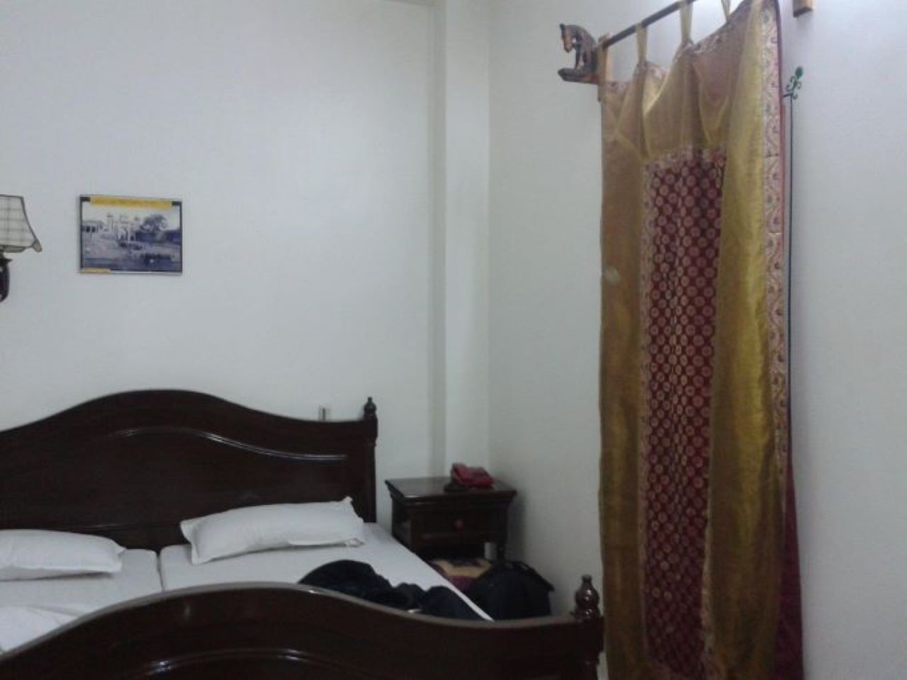 A bedroom with a wooden bed, a nightstand, a lamp, and a patterned curtain.