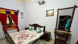 A bedroom with a bed, bedside table, mirror, and a small table with flowers. - Hotel Bharat Villas Jaisalmer (Jaisalmer)