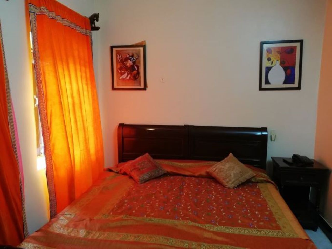 A bedroom with a bed, a nightstand, and two framed pictures on the wall.