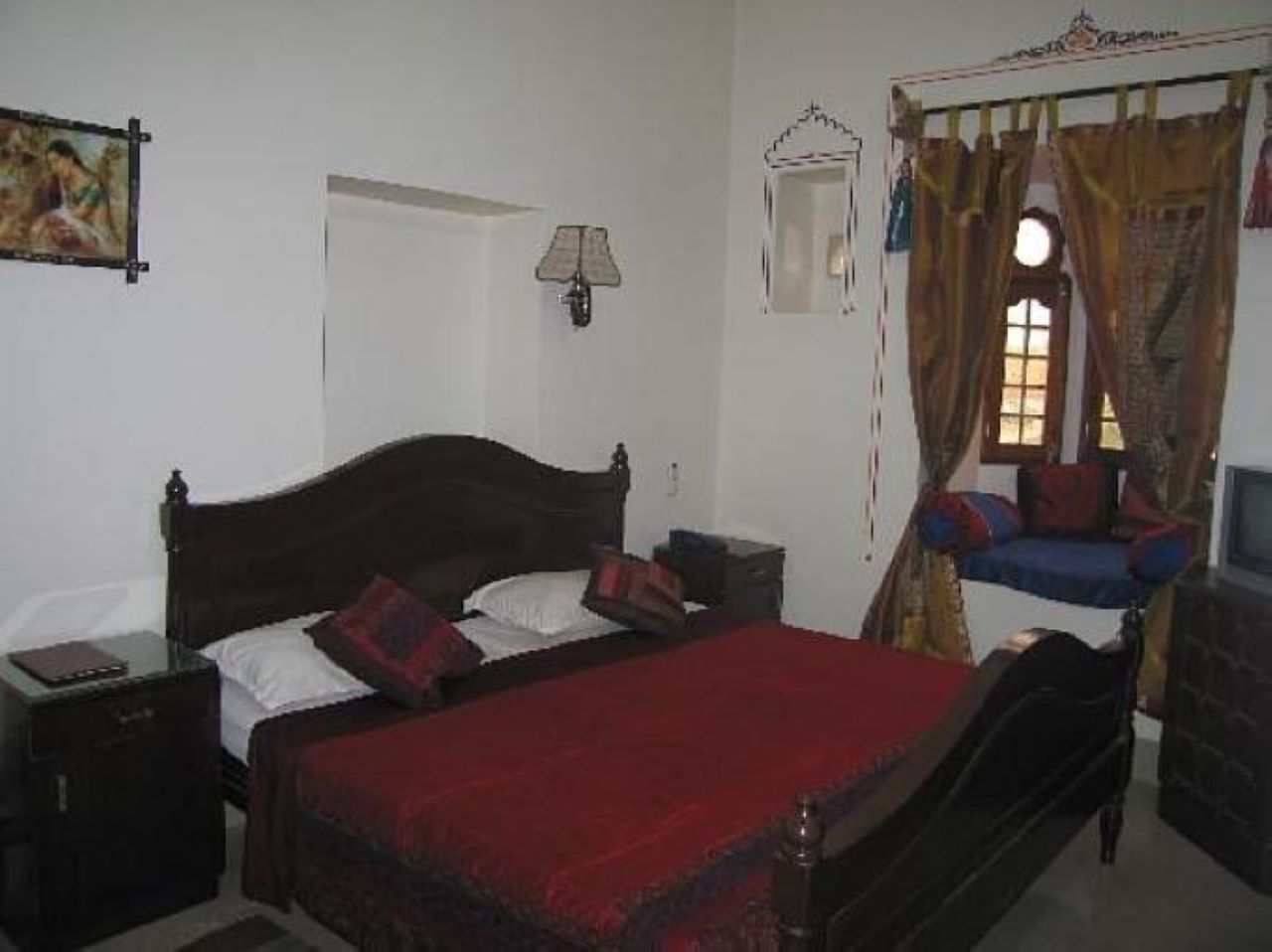 A bedroom with a wooden bed, a nightstand, a lamp, a window with curtains, and a television.