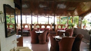 A restaurant with wooden ceiling, red cushioned chairs, and a large window overlooking greenery. - Hotel Bharat Villas Jaisalmer (Jaisalmer)