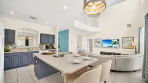 A modern kitchen with a central island, a dining area, and a living space with a sofa and TV. - Spacious Villa: Pool, Game Room & Themed Rooms (Kissimmee)