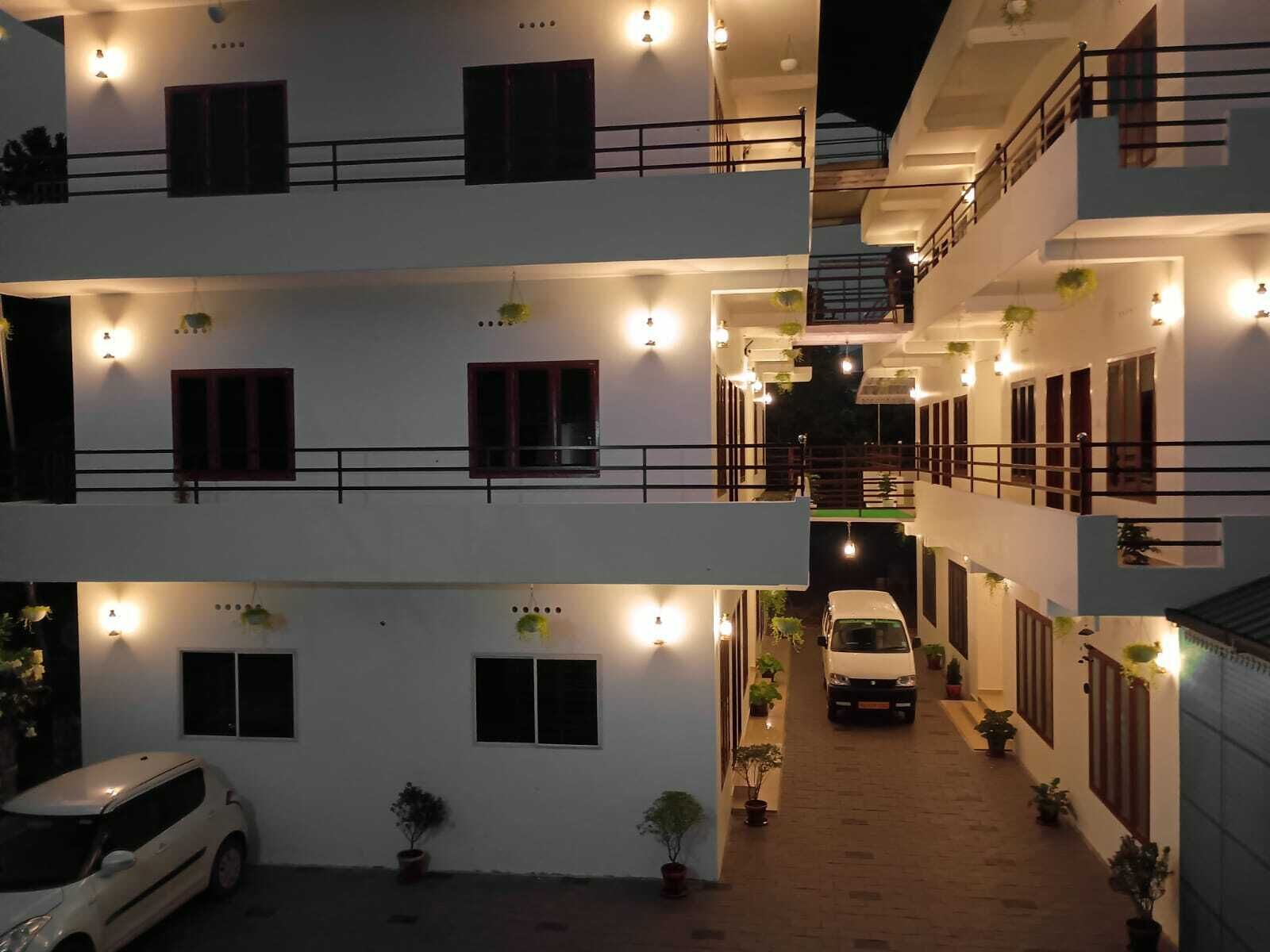 A multi-story building with balconies, potted plants, and a white car parked in the driveway.