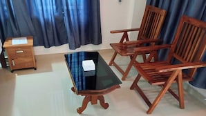 Une pièce avec une table à plateau en verre, deux chaises en bois, un petit meuble en bois et des rideaux bleus.
