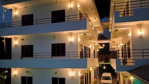 Un immeuble à plusieurs étages, doté de balcons, de plantes en pot et d’une voiture blanche garée devant.