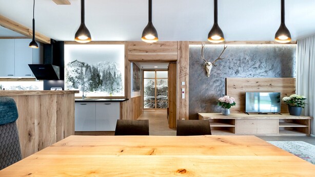 A modern kitchen with a wooden island, a dining area with a large wooden table, and a living space with a TV and decorative items. - Lively apartment near the ski slope (Schladming - Rohrmoos)