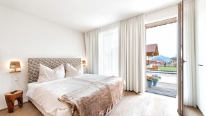 A bedroom with a large bed, a nightstand, and a view of a building through a sliding door. - Lively apartment near the ski slope (Schladming - Rohrmoos)