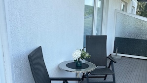 A balcony with a round table and four chairs, a small vase with flowers, and a view of the sea. - Vacation apartment Menges (Medebach)