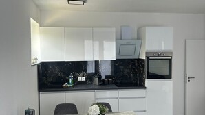 A modern kitchen with white cabinets, a black countertop, and a dining area with two chairs and a table. - Vacation apartment Menges (Medebach)