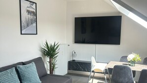 A modern living room with a sofa, a coffee table, a dining area with chairs, a TV mounted on the wall, and a framed picture. - Ferienwohnung Juli - neu Renovierte, Moderne Ferienwohnung (Medebach)
