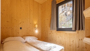 Ein Zimmer mit Holzwänden, einem Bett, einem Fenster mit Vorhängen und einer Wandleuchte.
