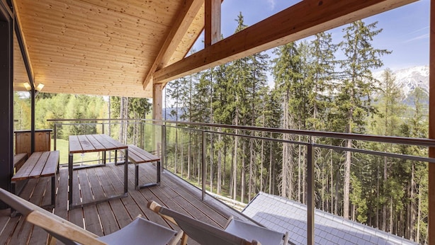 Eine Holterrasse mit Picknicktischen und -stühlen, mit Blick auf einen Wald und Berge.
