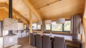 Eine moderne Küche mit Kamin aus Stein, Holzbalken und großen Fenstern.