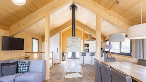 Ein geräumiges Blockhütten-Interieur mit Holzbalkendecke, Kamin aus Stein, Essbereich und Küche.