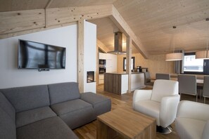 A modern interior with a grey sectional sofa, white armchairs, a wooden coffee table, and a kitchen area with a central island. - Nice chalet with balconies (Schladming - Pichl, Ennstal)