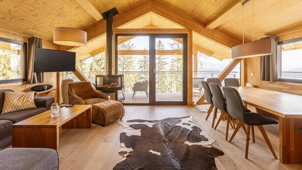 Ein gemütliches Holzhaus-Interieur mit einem großen Esstisch, einer Ledersofa und einem Fernseher.