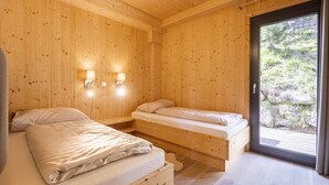 Ein Schlafzimmer einer Holzhütte mit zwei Betten, einer Schiebetür zu einem Balkon und Wandleuchten.