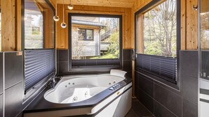 A modern bathroom with a large bathtub, wooden walls, and large windows offering a view of a house and trees. - Appealing chalet with sauna (Schladming - Pichl, Ennstal)