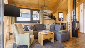 A cozy cabin interior with a wooden ceiling, a gray sofa, a small armchair, a wooden coffee table, and a fireplace. - Appealing chalet with sauna (Schladming - Pichl, Ennstal)