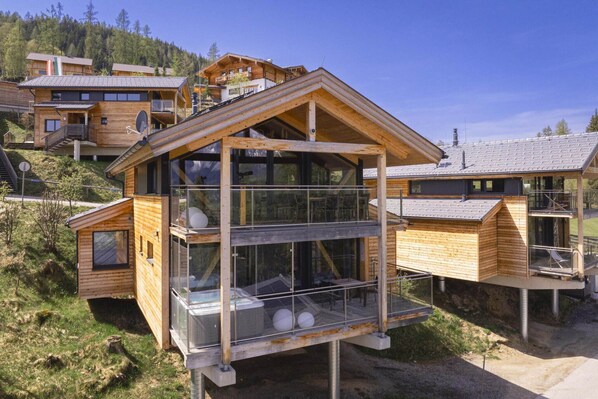 Une cabane moderne en bois, dotée d’un balcon en verre, d’un jacuzzi et, au loin, d’un télésiège.