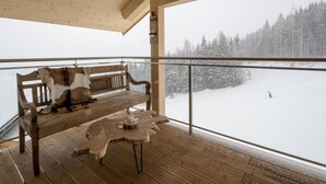 Un banco y una mesa de madera en un balcón con vistas a un paisaje nevado.