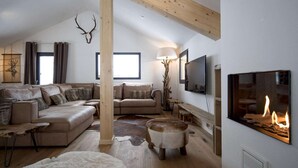 Un salón espacioso con techo alto, chimenea, televisor montado y un amplio ventanal.